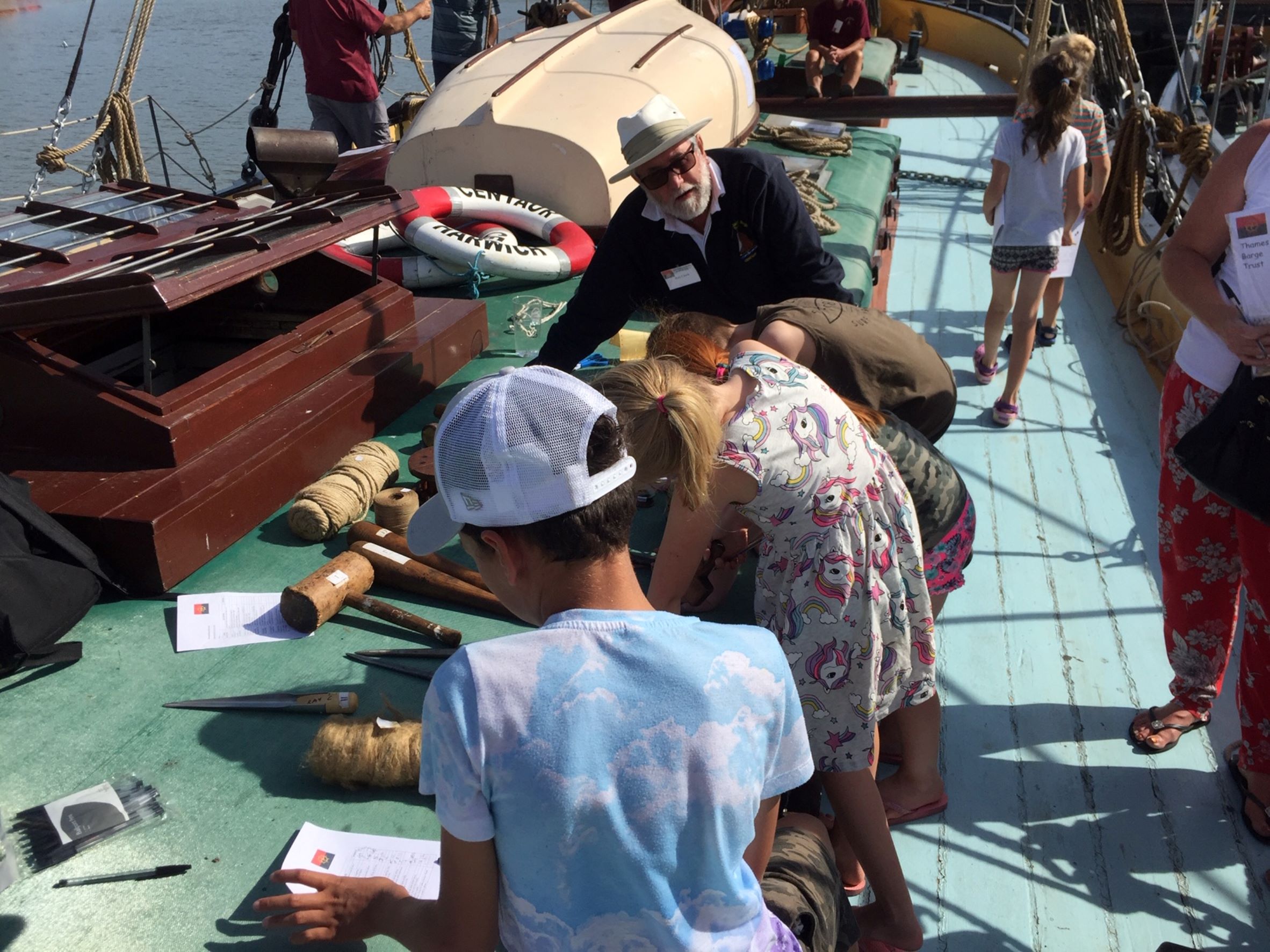 Children engaged in an activity, bend over the hold cover of SB Centaur, with one of the TSBT volunteers supervising the task