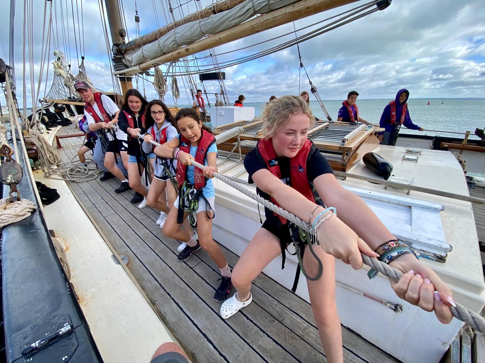 Seven young people pulling ropes on board Queen Galadriel