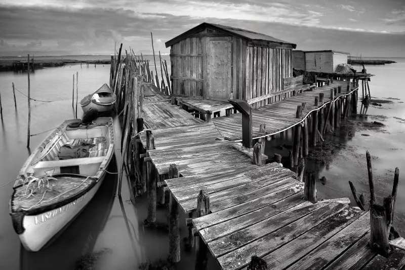 Black and white photo of a pier with small boats moored alongside