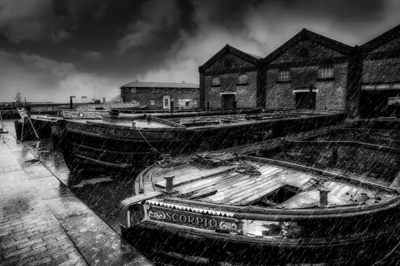 Black and white view of rain pouring down over moored up vessels
