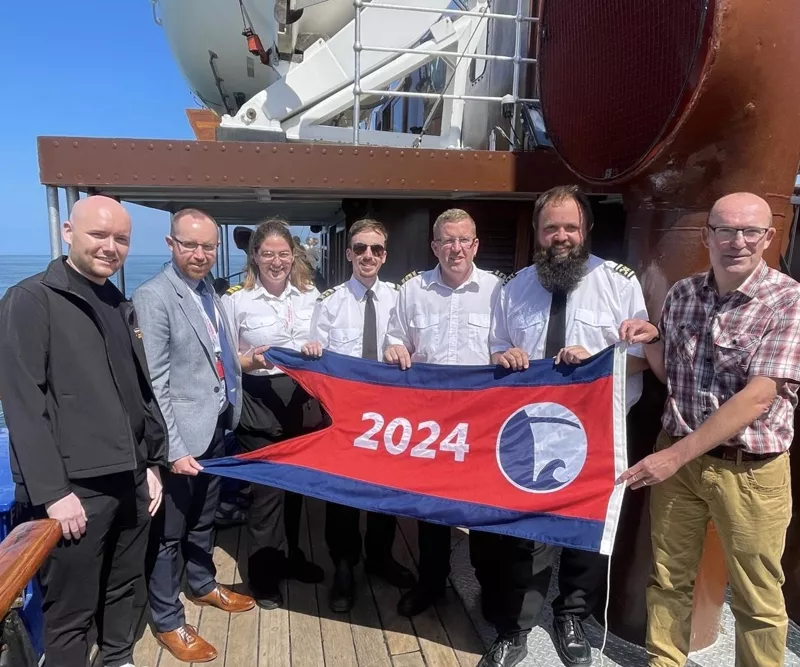 Waverley team standing in line on board the ship and presenting the flag they've received as the Flagship of the Year